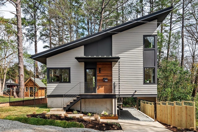 contemporary home featuring stairway, board and batten siding, gravel driveway, and fence