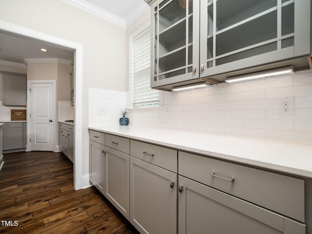 kitchen featuring decorative backsplash, gray cabinets, dark wood finished floors, crown molding, and glass insert cabinets