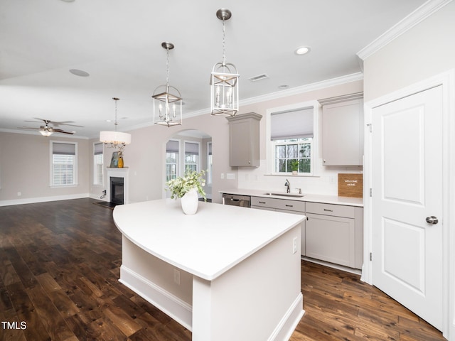 kitchen featuring gray cabinetry, light countertops, stainless steel dishwasher, a glass covered fireplace, and a sink