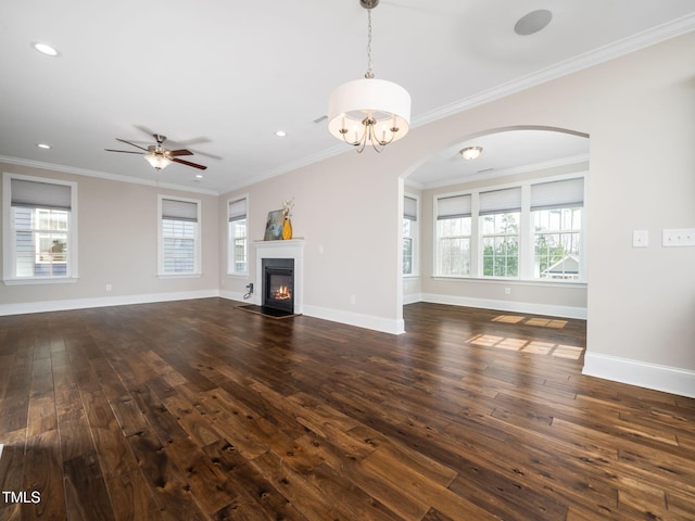 unfurnished living room with arched walkways, crown molding, dark wood-type flooring, and baseboards