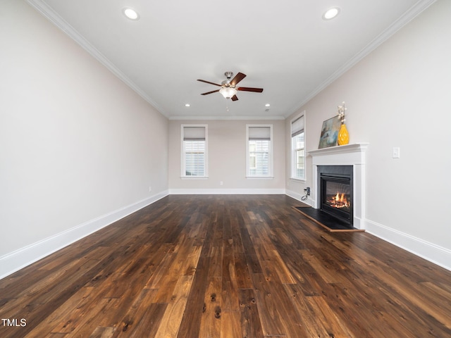 unfurnished living room with crown molding, dark wood-type flooring, baseboards, a glass covered fireplace, and a ceiling fan