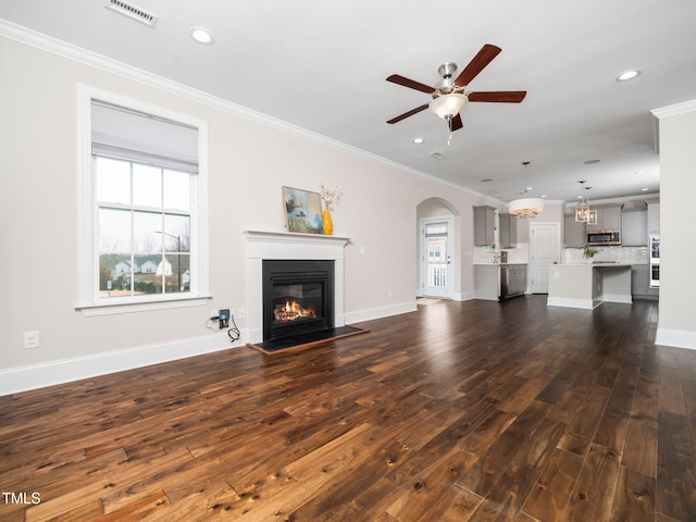 unfurnished living room with a wealth of natural light, visible vents, ceiling fan with notable chandelier, and ornamental molding