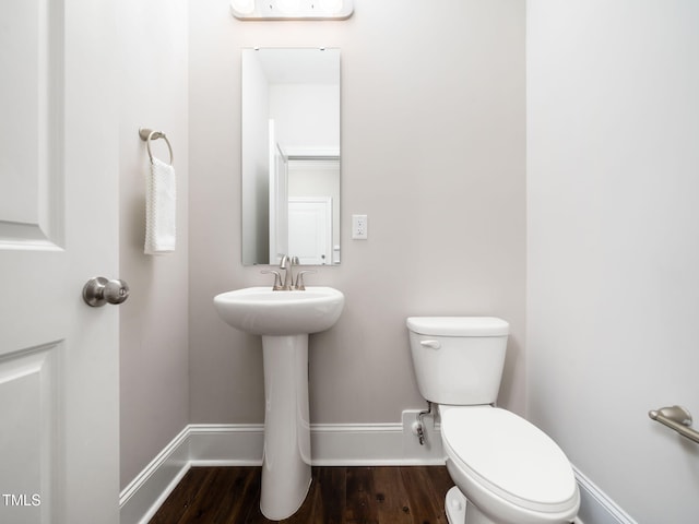 half bathroom with toilet, wood finished floors, and baseboards