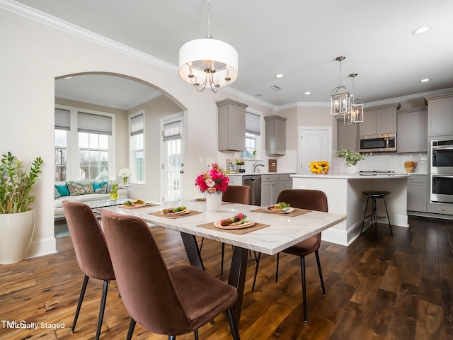 dining space featuring dark wood finished floors, an inviting chandelier, arched walkways, and ornamental molding