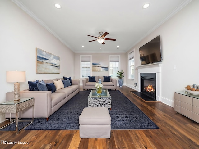 living area with baseboards, ornamental molding, wood finished floors, a glass covered fireplace, and a ceiling fan