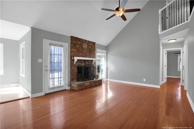 unfurnished living room featuring a stone fireplace, baseboards, wood-type flooring, and high vaulted ceiling