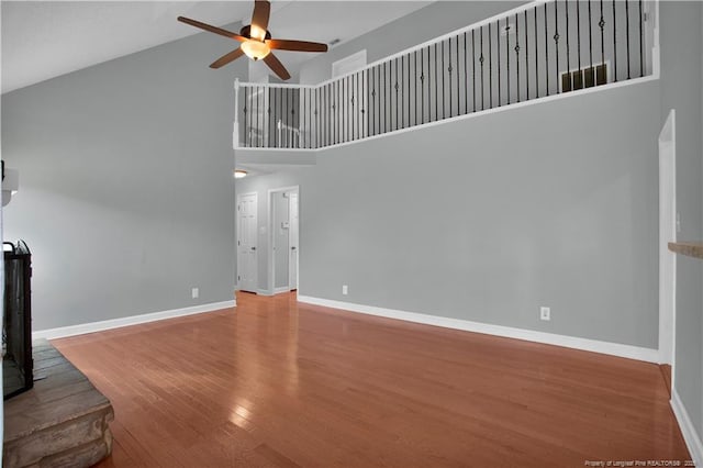 unfurnished living room with a ceiling fan, wood finished floors, baseboards, and high vaulted ceiling