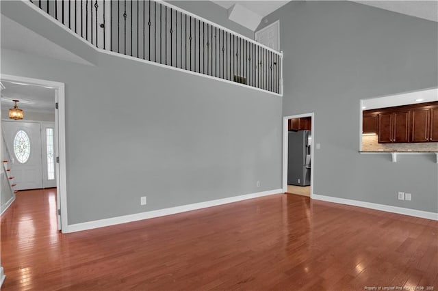 unfurnished living room with high vaulted ceiling, baseboards, and hardwood / wood-style flooring