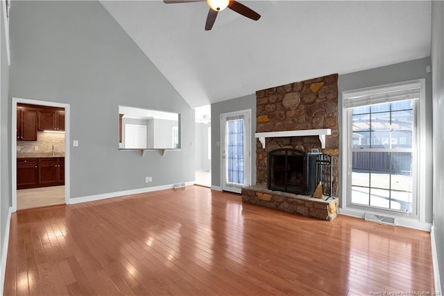 unfurnished living room featuring visible vents, high vaulted ceiling, wood-type flooring, a fireplace, and baseboards