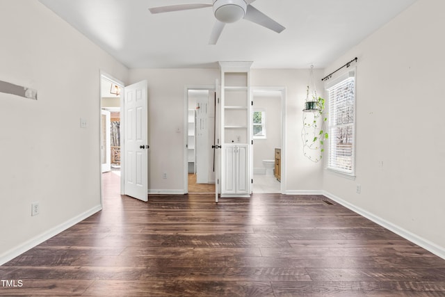 unfurnished bedroom with dark wood-style floors, baseboards, ensuite bathroom, and ceiling fan