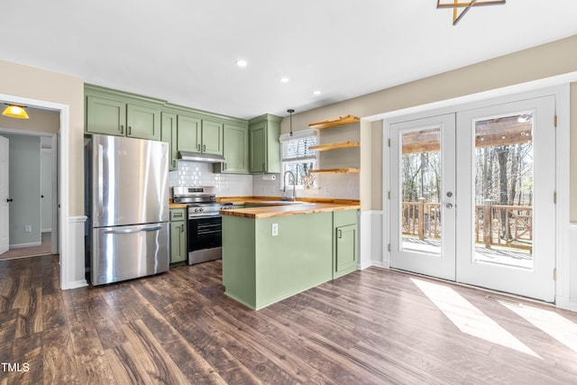 kitchen with under cabinet range hood, stainless steel appliances, a peninsula, green cabinets, and butcher block counters