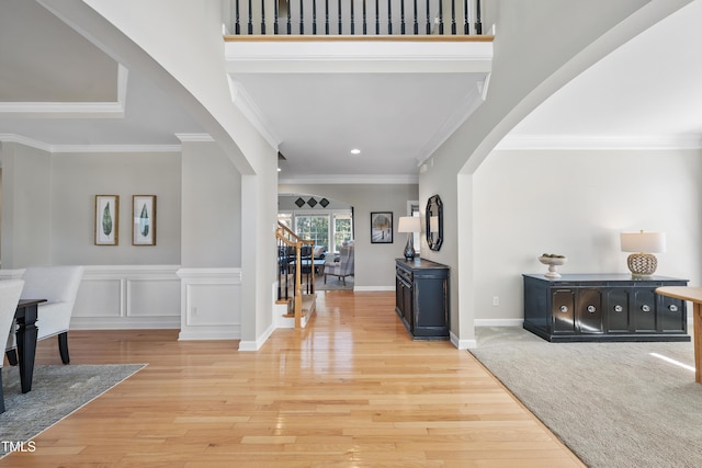 foyer with baseboards, light wood finished floors, arched walkways, stairs, and crown molding