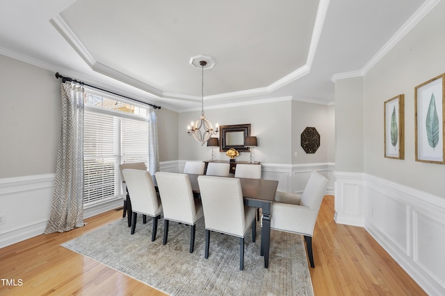 dining space with a wainscoted wall, an inviting chandelier, crown molding, a raised ceiling, and light wood-type flooring