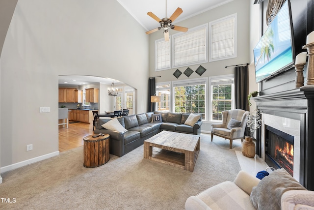 living area with light carpet, a fireplace with flush hearth, ceiling fan with notable chandelier, arched walkways, and baseboards