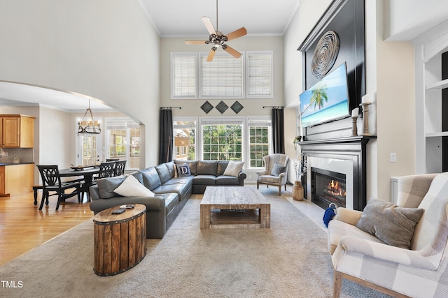 living area featuring light wood-type flooring, a fireplace with flush hearth, ceiling fan with notable chandelier, arched walkways, and crown molding