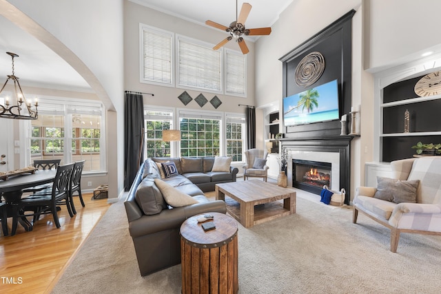 living area with light wood-style flooring, ceiling fan with notable chandelier, a glass covered fireplace, arched walkways, and crown molding