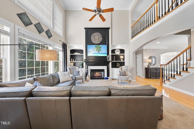 living room featuring ornamental molding, wood finished floors, a glass covered fireplace, arched walkways, and ceiling fan