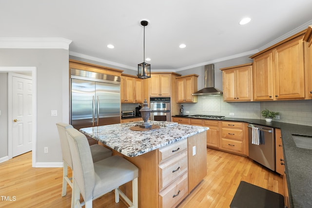 kitchen with wall chimney range hood, light wood finished floors, appliances with stainless steel finishes, and a center island