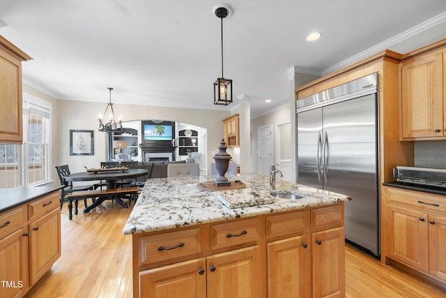 kitchen featuring a kitchen island, a fireplace, a sink, ornamental molding, and stainless steel built in refrigerator