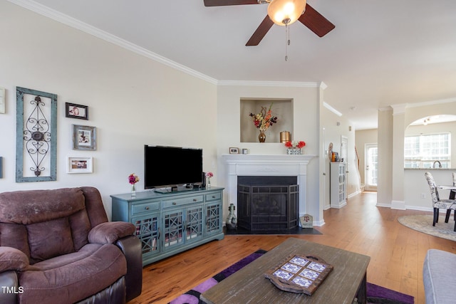 living room with hardwood / wood-style floors, a ceiling fan, baseboards, a fireplace with flush hearth, and ornamental molding