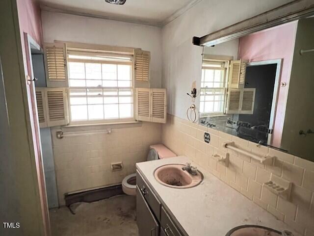 bathroom featuring tile walls, toilet, double vanity, and a sink