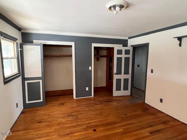 unfurnished bedroom with wood finished floors, multiple closets, and ornamental molding