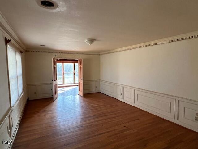 empty room with crown molding, a decorative wall, wood finished floors, and a wainscoted wall