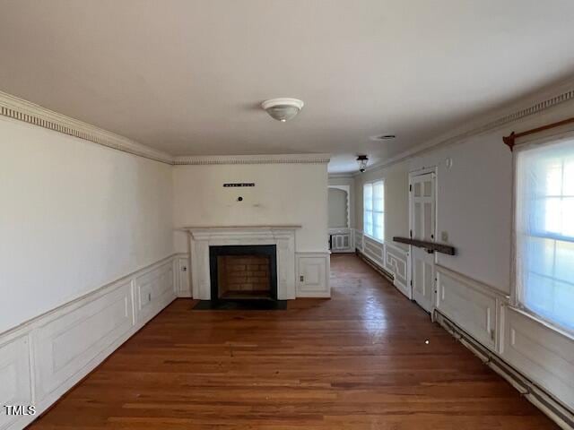 unfurnished living room with a wainscoted wall, a fireplace with flush hearth, ornamental molding, wood finished floors, and a decorative wall