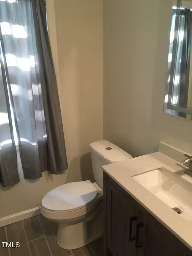 bathroom with wood finish floors, baseboards, toilet, and vanity