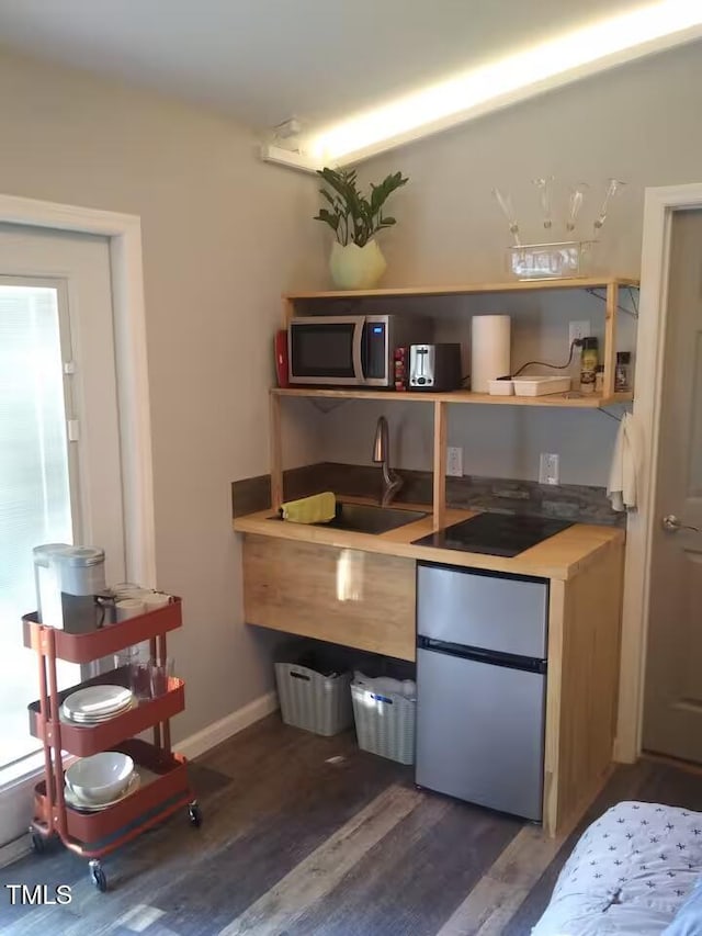 kitchen with a sink, appliances with stainless steel finishes, baseboards, and wood finished floors