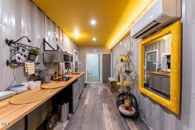 kitchen with a wall mounted AC, dark wood-style flooring, stainless steel appliances, a sink, and light countertops