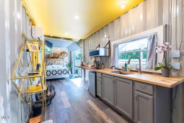 kitchen featuring a sink, gray cabinetry, dark wood-type flooring, butcher block countertops, and stainless steel dishwasher