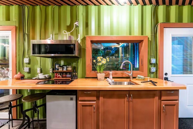 kitchen with stainless steel microwave, wallpapered walls, black electric stovetop, butcher block counters, and a sink