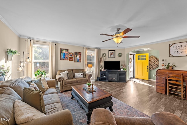 living room featuring wood finished floors, baseboards, arched walkways, ceiling fan, and crown molding