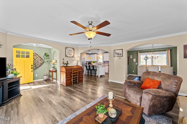 living area featuring wood finished floors, baseboards, arched walkways, ornamental molding, and ceiling fan with notable chandelier