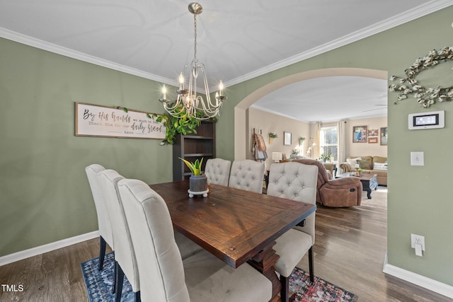 dining space with arched walkways, crown molding, baseboards, and wood finished floors