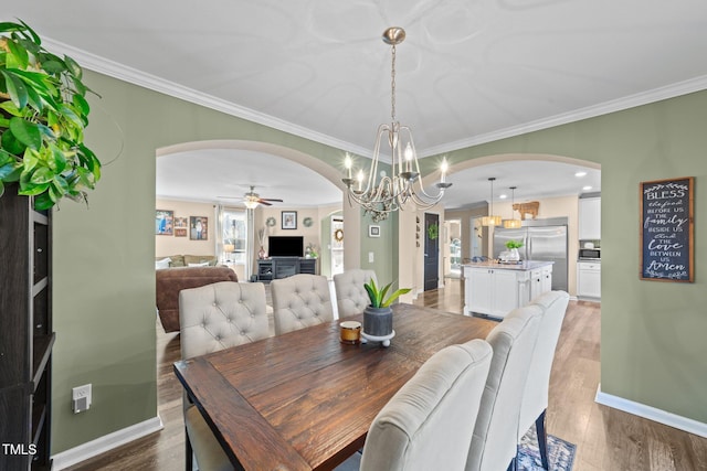 dining room featuring crown molding, baseboards, arched walkways, and light wood-type flooring