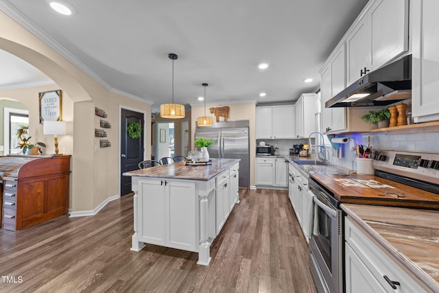 kitchen featuring arched walkways, a sink, appliances with stainless steel finishes, under cabinet range hood, and a center island