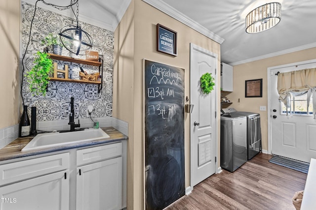 washroom with cabinet space, washer and dryer, crown molding, and a sink