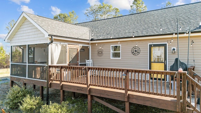 back of property with a deck, a sunroom, and a shingled roof