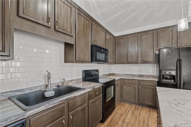 kitchen featuring backsplash, light wood-style flooring, hanging light fixtures, black appliances, and a sink