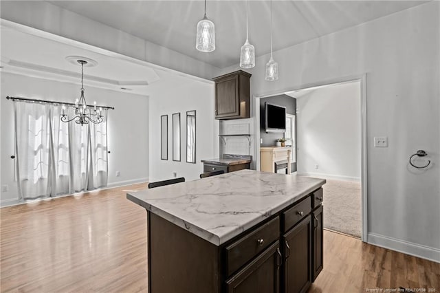 kitchen with light wood-type flooring, decorative light fixtures, a tray ceiling, dark brown cabinetry, and baseboards