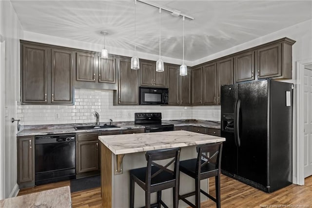 kitchen with black appliances, a sink, a kitchen island, wood finished floors, and dark brown cabinetry