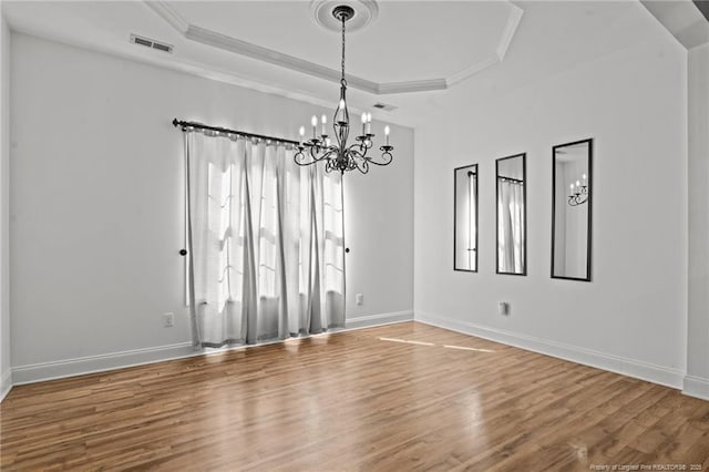 spare room featuring visible vents, a raised ceiling, wood finished floors, and crown molding