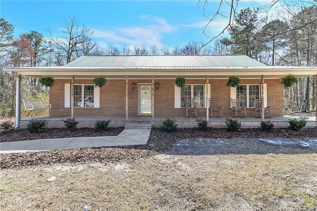 single story home with metal roof, brick siding, and a porch