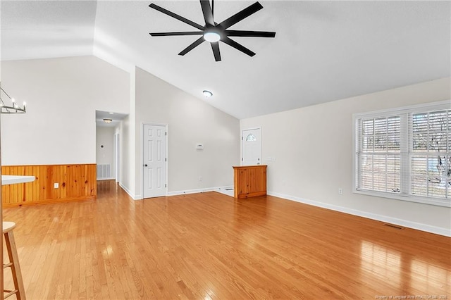 unfurnished living room featuring ceiling fan with notable chandelier, light wood-style floors, visible vents, and high vaulted ceiling