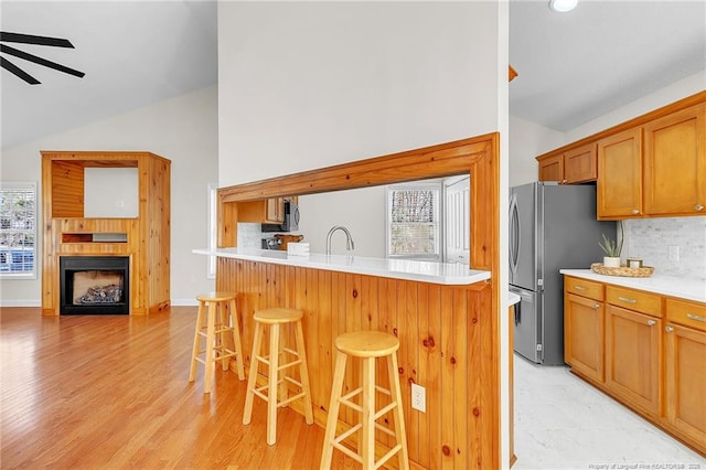 kitchen featuring a kitchen bar, a ceiling fan, a sink, a fireplace, and light countertops