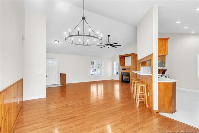 unfurnished living room with light wood finished floors, baseboards, ceiling fan with notable chandelier, a fireplace, and high vaulted ceiling