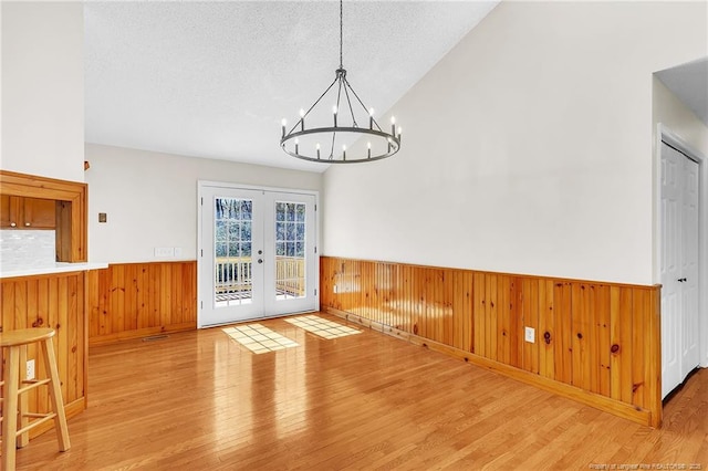 unfurnished dining area featuring wooden walls, wainscoting, french doors, and vaulted ceiling