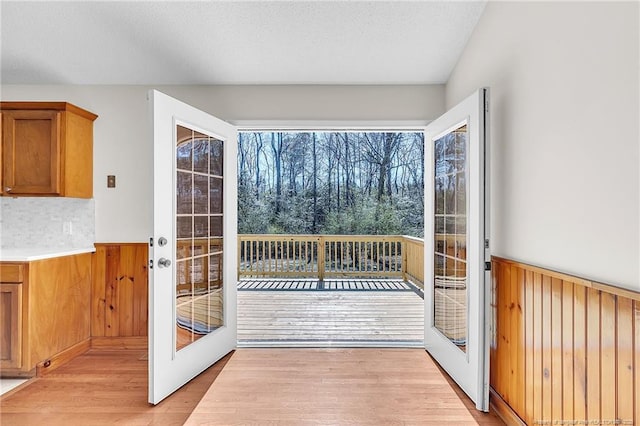 doorway with a wainscoted wall, light wood-style flooring, french doors, and a textured ceiling